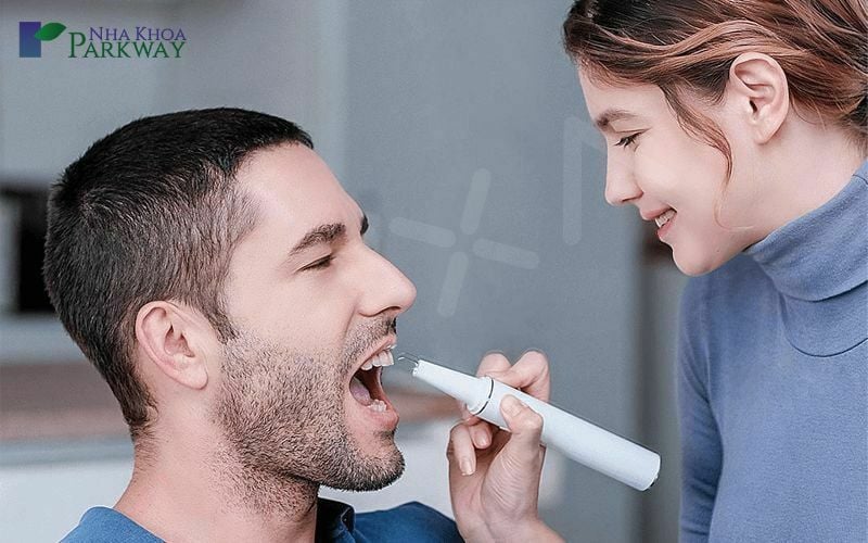 Cô gái sử dụng máy lấy cao răng để vệ sinh răng miệng cho chồng tại nhà
