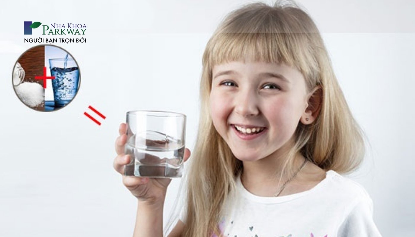 Hình ảnh bé gái cầm ly nước muối loãng để súc miệng