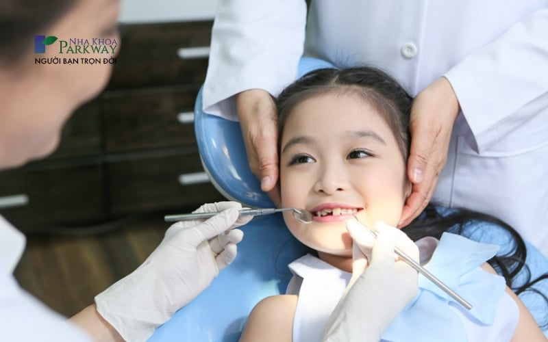 Hình ảnh bác sĩ nha khoa dùng công cụ chuyên dụng để khám răng cho bé gái