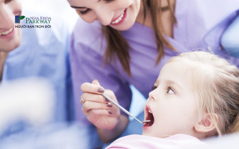 Bác sĩ đang kiểm tra tình trạng răng miệng cho bé gái bằng công cụ nha khoa
